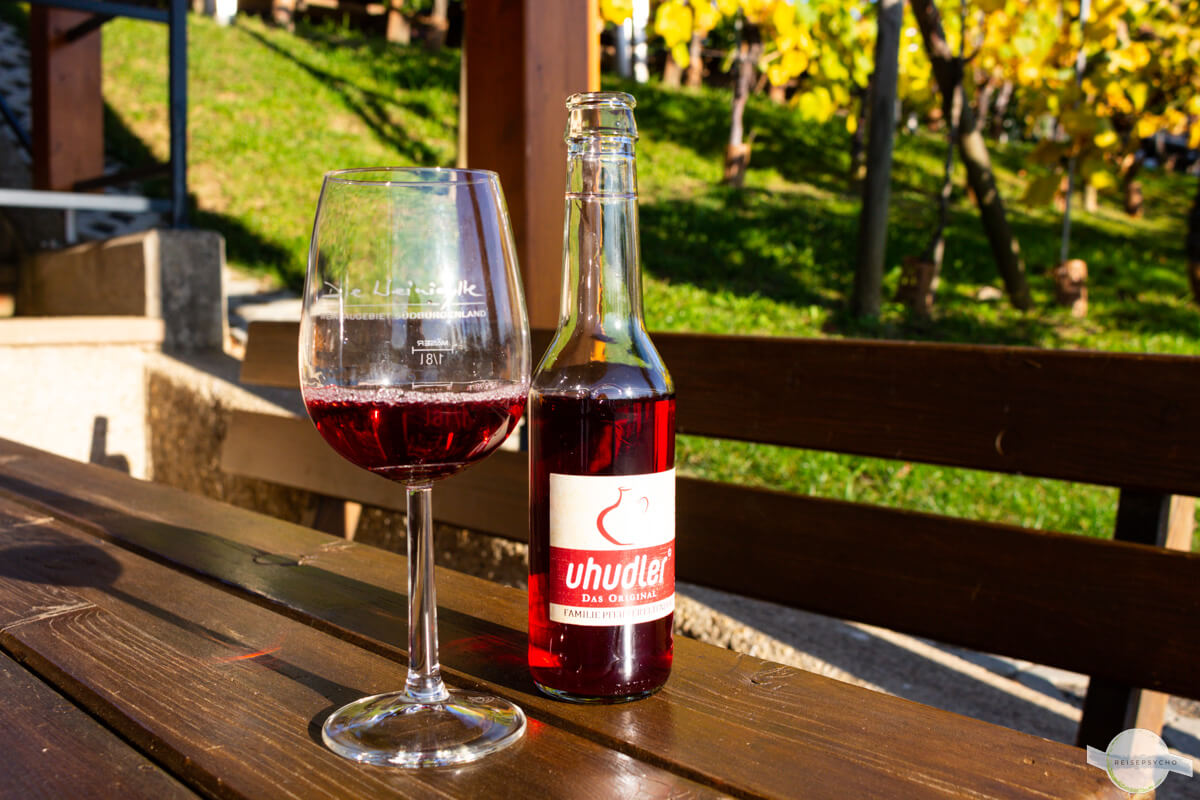 Uhudler in kleiner Flasche und im Glas, dahinter der Weingarten