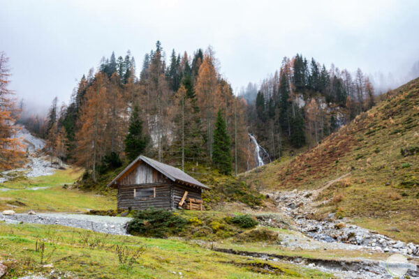 Hütte, dahinter ein Wasserfall und Wald