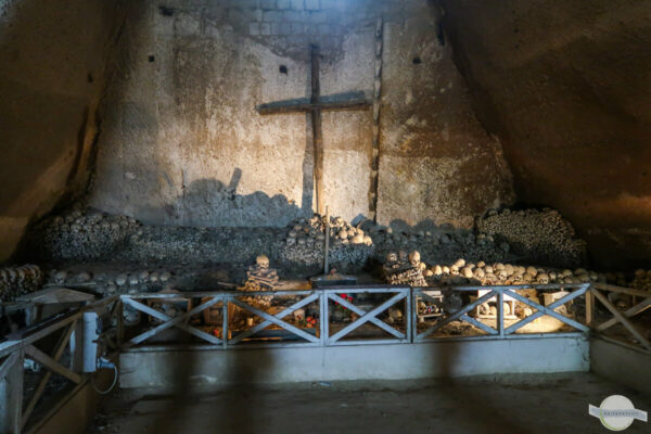 Holzkreuz in Höhle, umgeben von Totenschädeln