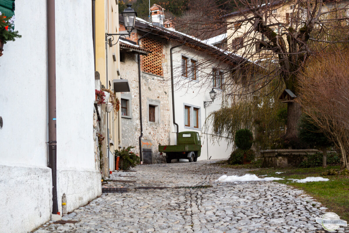 Alte gepflasterte Gasse, vor einem Haus steht eine grüne Ape