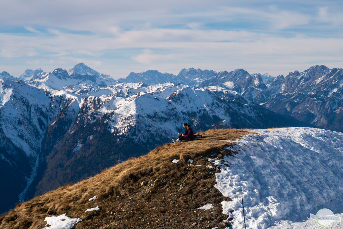 Sitzen am Berggipfel im Winter, dahinter Bergpanorama