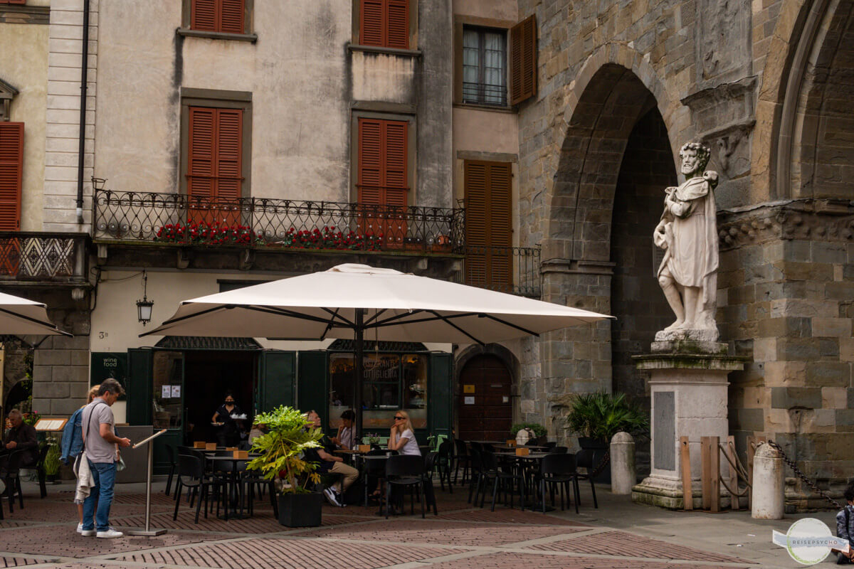 Alte Gebäude und ein großer Sonnenschirm, darunter eine Trattoria